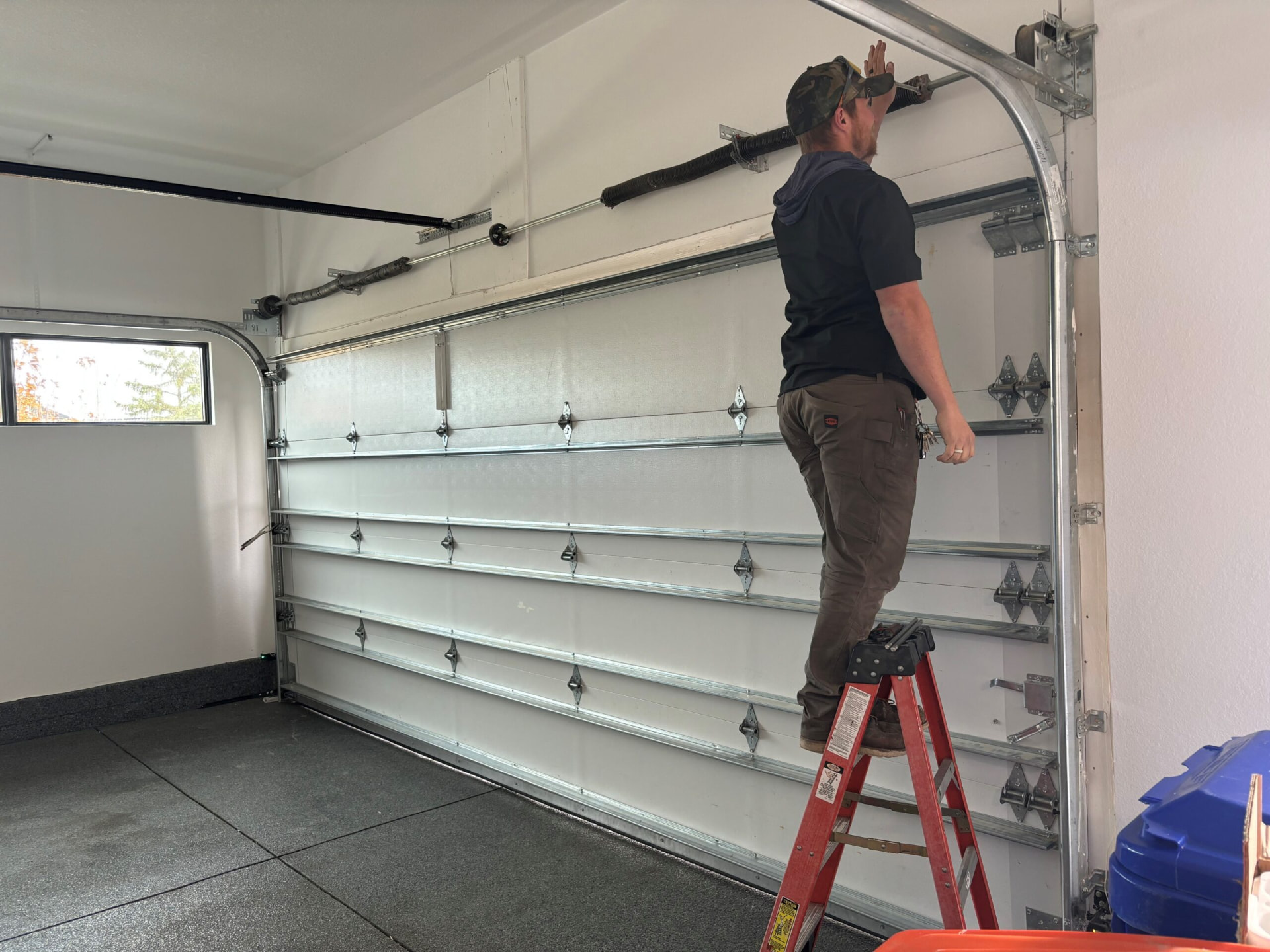Technician on a ladder working near the garage door cable drum