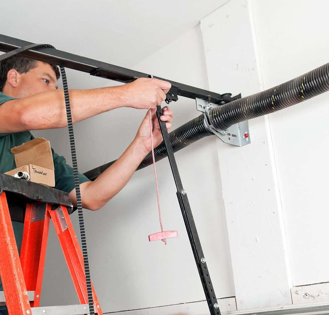Technician on a ladder working on garage door hardware near the spring