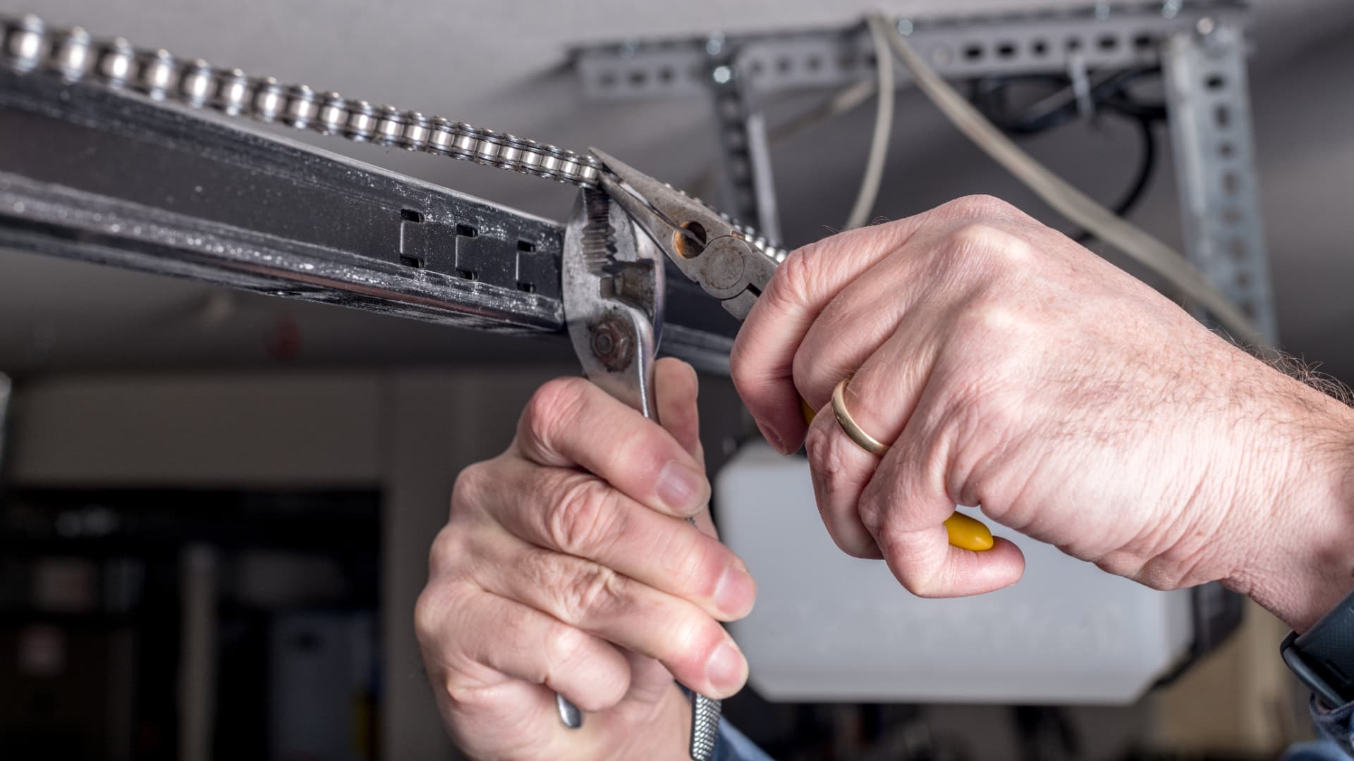Hands adjusting garage door hardware with pliers