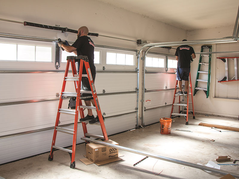 Two technicians on ladders working on garage door tracks